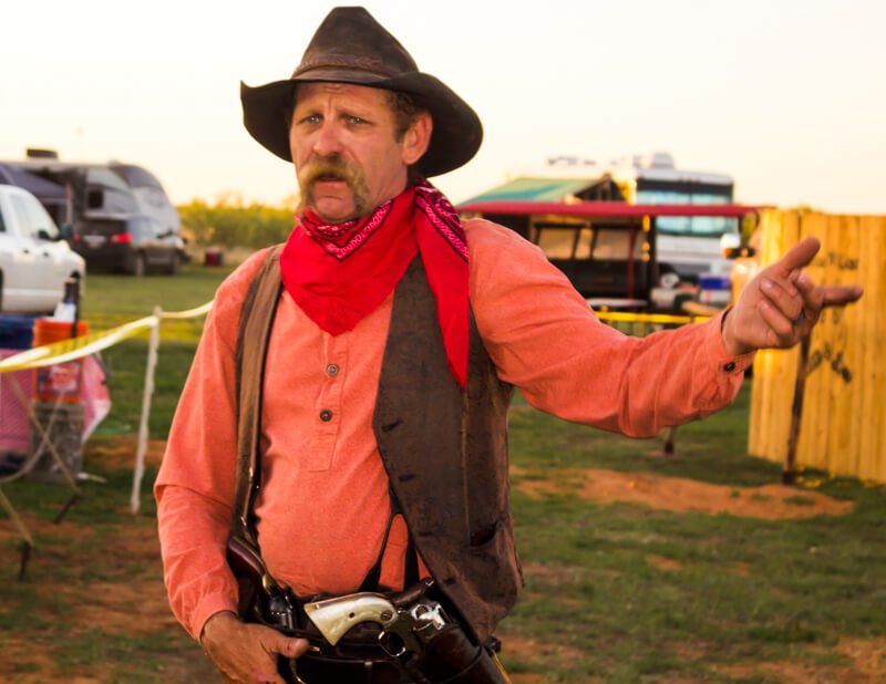 A man in cowboy gear and red shirt holding a camera.